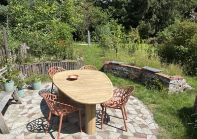 Terras van gebroken natuursteen met houten tuintafel en terracotta stoelen