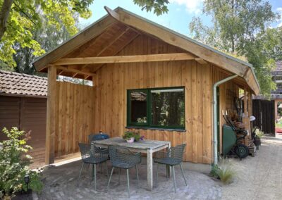 Overkapping van de tuinschuur met houten eettafel en groene stoelen