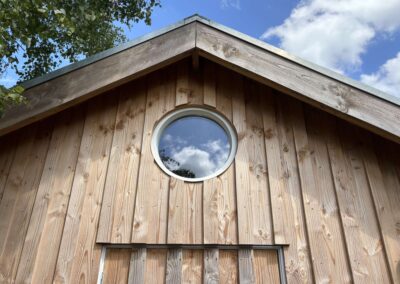 Topgevel van de tuinschuur met rond raam in verticale houten delen